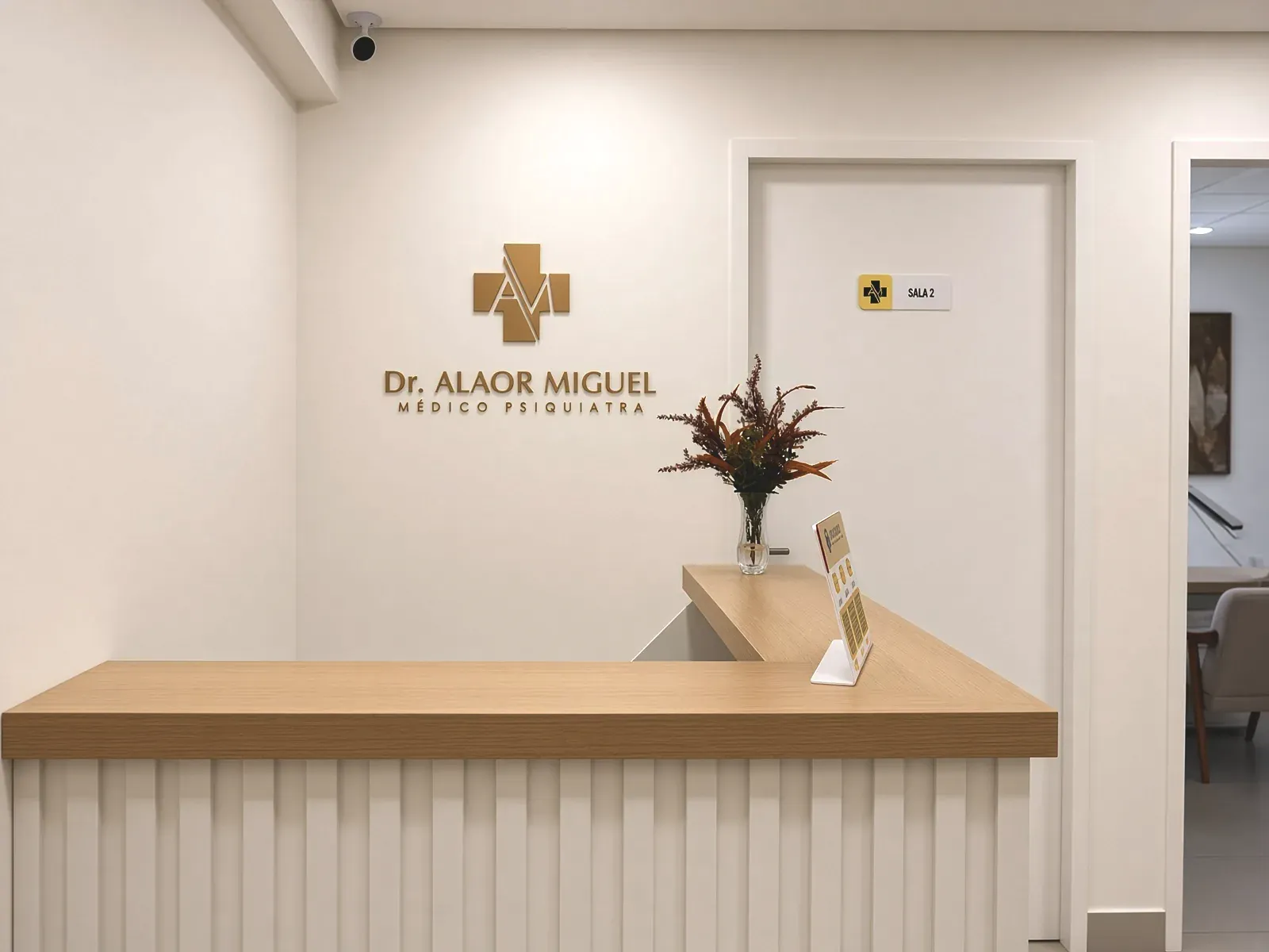 Balcão de recepção em madeira clara com a identidade Dr. Alaor Miguel aplicada na parede